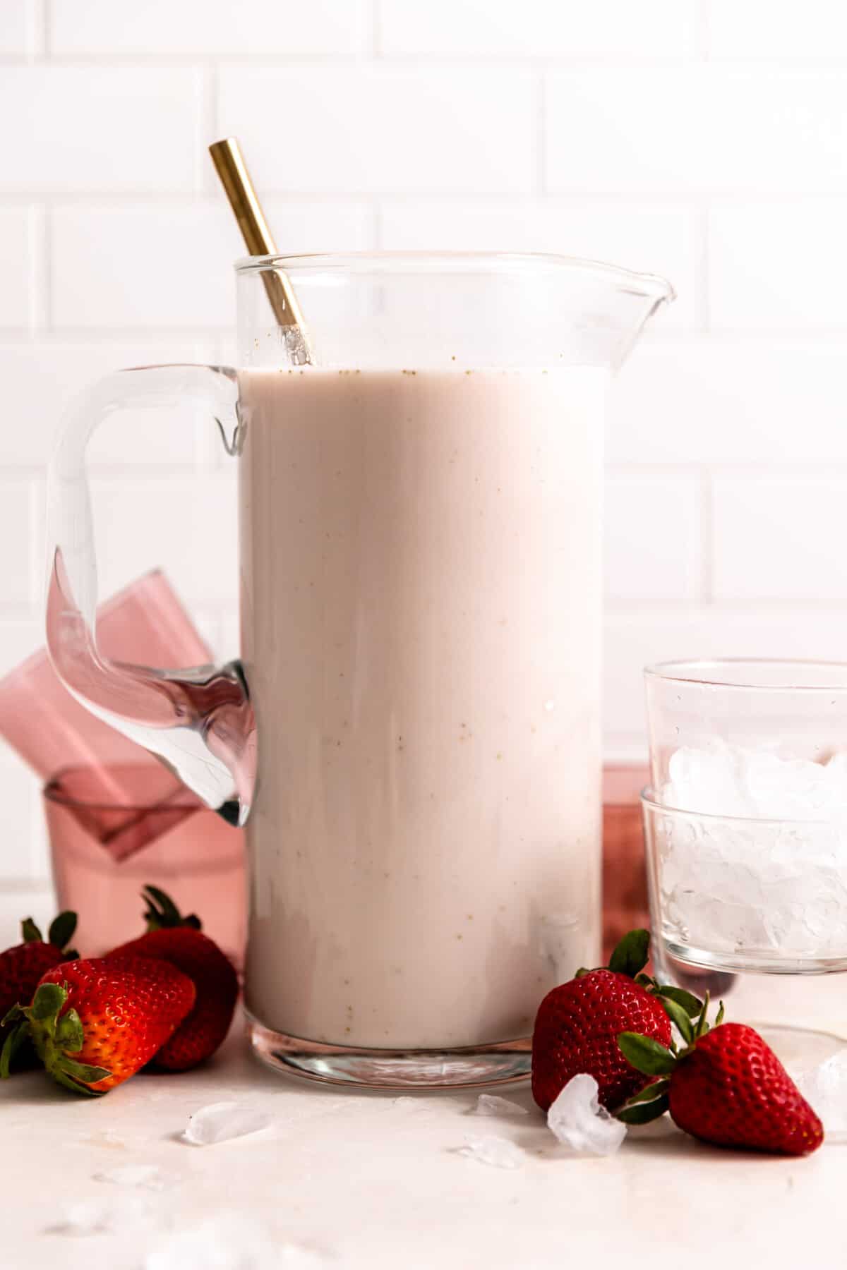 Pitcher filled with pink strawberry horchata with a spoon inside.
