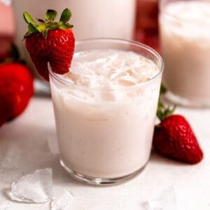 Small glass filled with light pink, strawberry horchata, with a strawberry on the rim of the glass as a garnish.