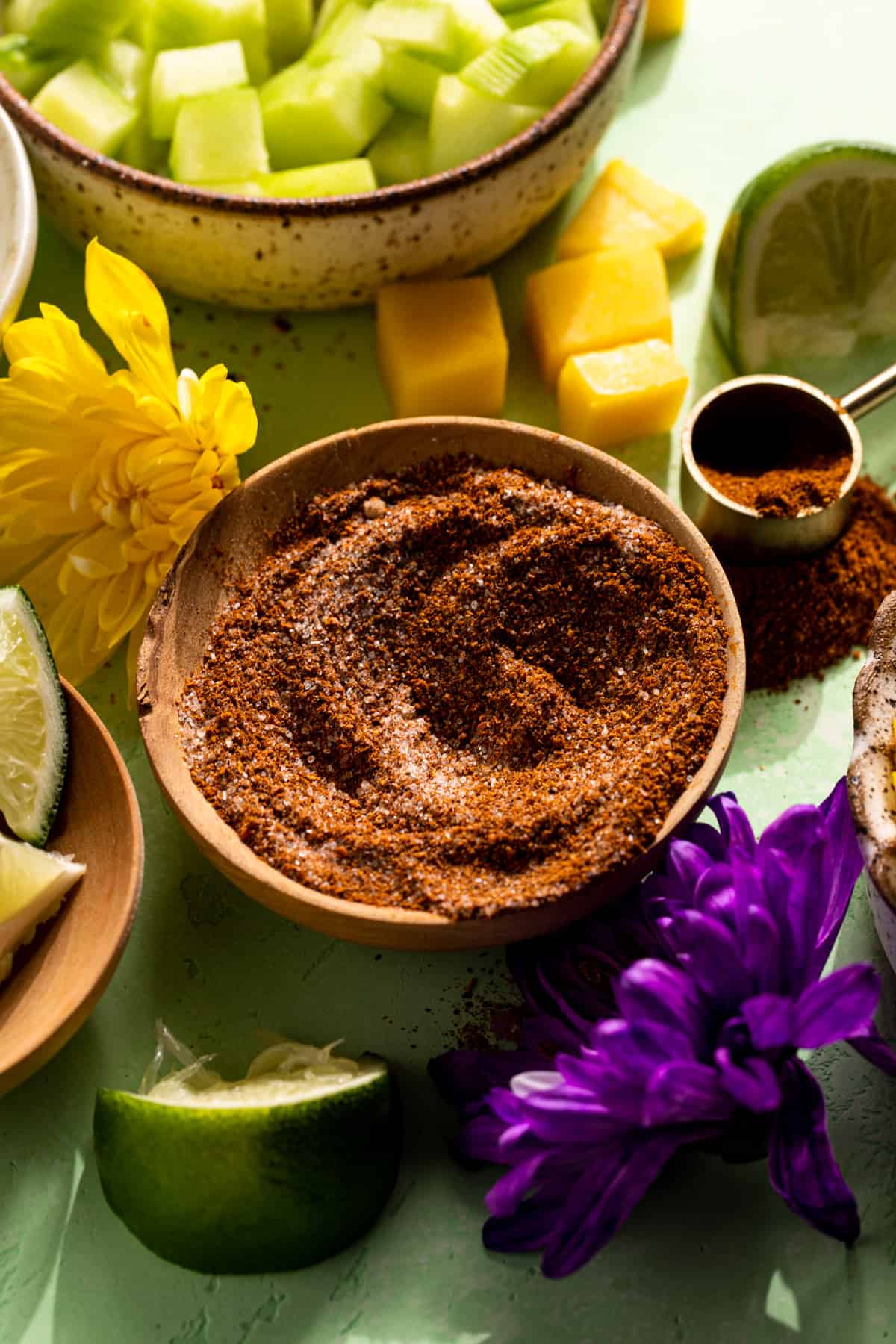 Small wooden bowl with chili lime seasoning, surrounded by chopped cucumber and fruits.