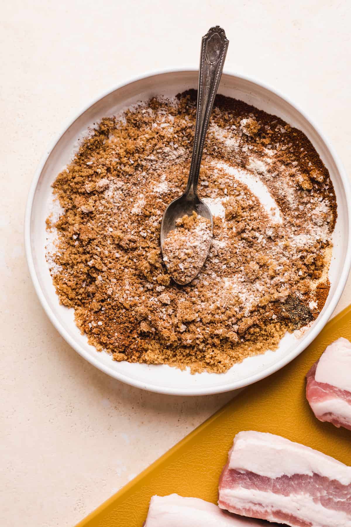 Bowl of ingredients for a sweet pork rub stirred with a spoon.