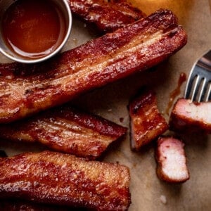 Strips of smoked pork belly on brown parchment paper with a small bowl of BBQ sauce and a beer.