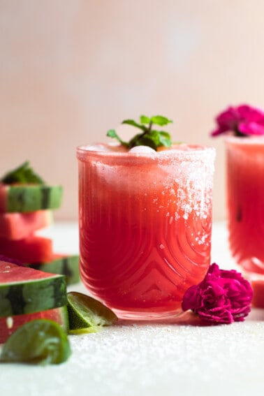 Glass with watermelon margarita garnished with a sprig of mint and salt on the rim.