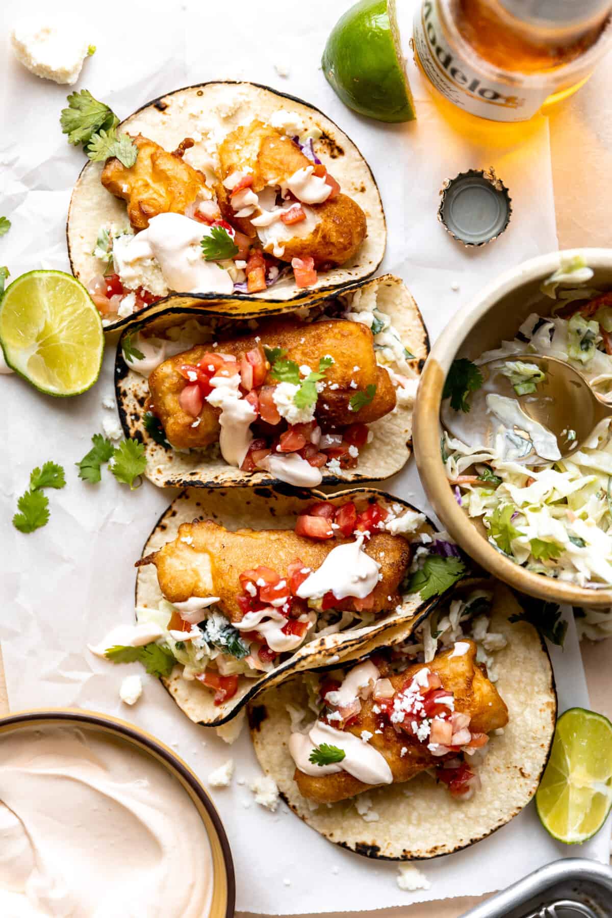 Baja fish tacos served with a bowl of fish taco slaw on the side and a beer. 