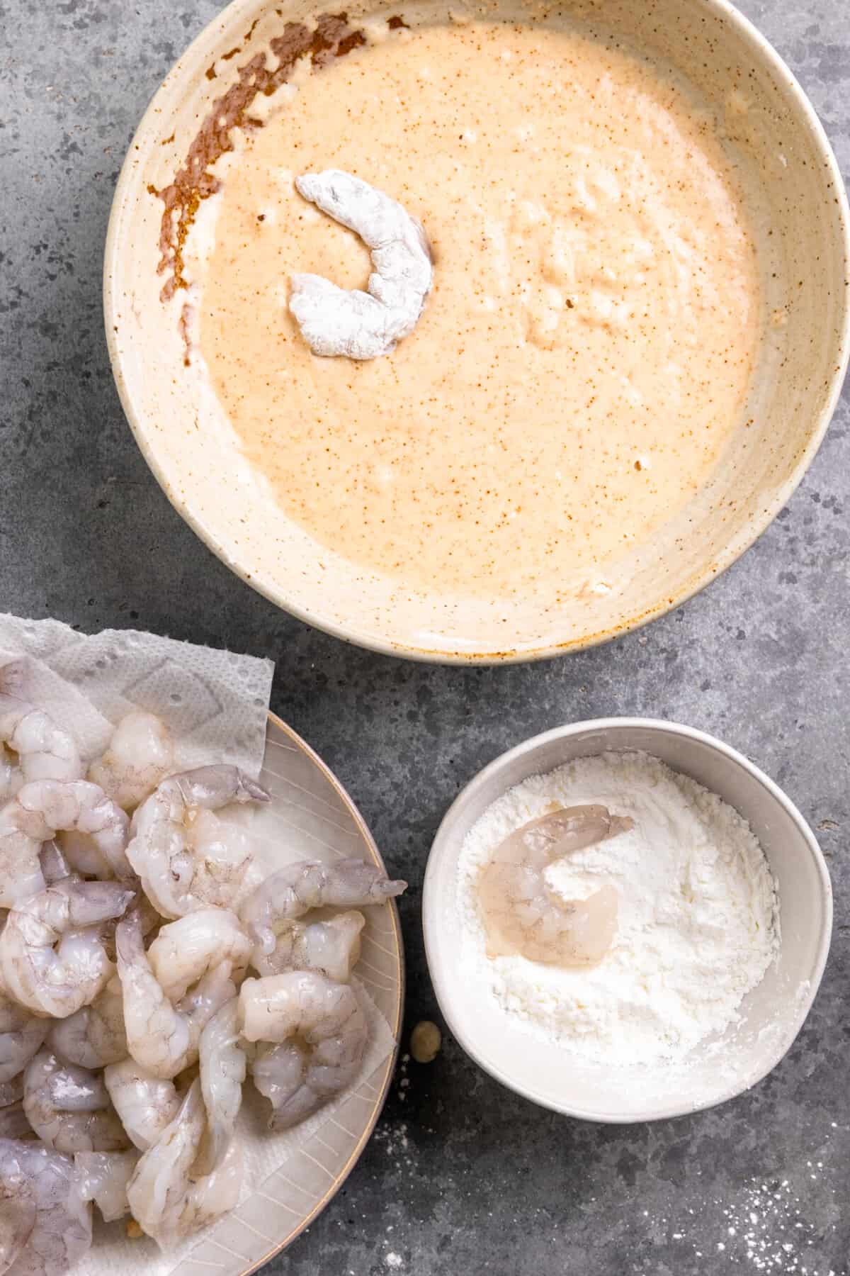 Shrimp being dipped into a bowl of cornstarch and then into a bowl of beer batter.