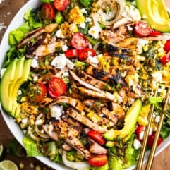 Salad in a white bowl topped with grilled chicken, peppers, and onion plus other ingredients.