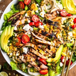 Salad in a white bowl topped with grilled chicken, peppers, and onion plus other ingredients.