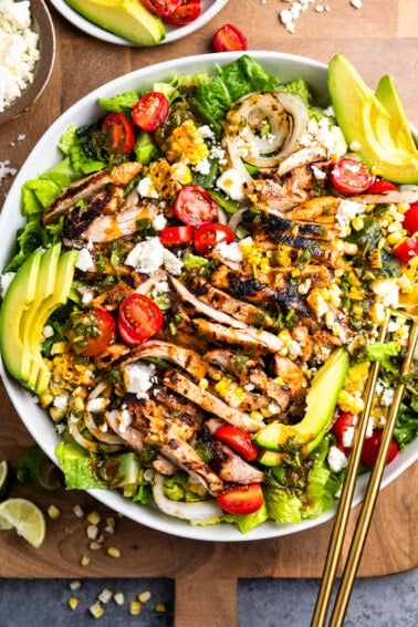 Salad in a white bowl topped with grilled chicken, peppers, and onion plus other ingredients.