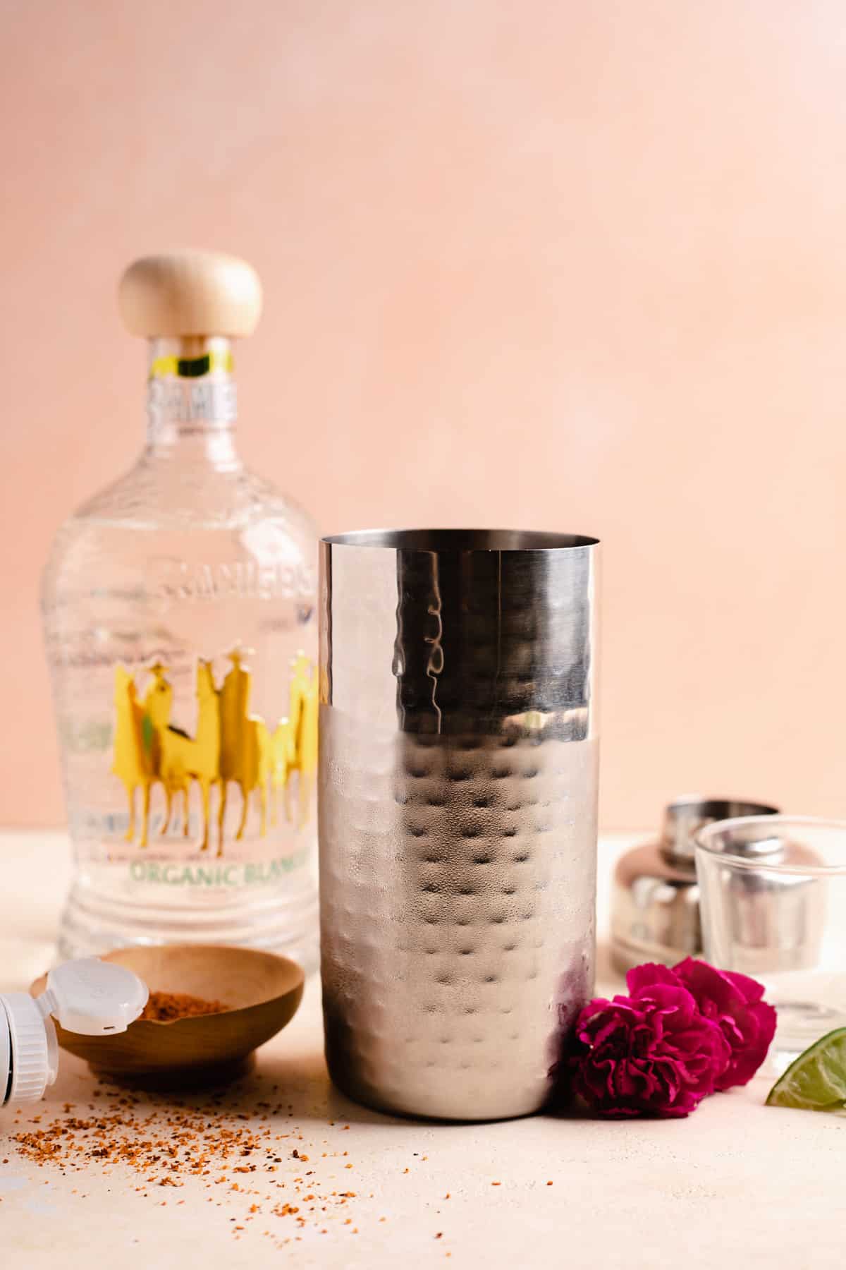 Cocktail shaker with a bottle of tequila, and a bowl of tajin on the side. 