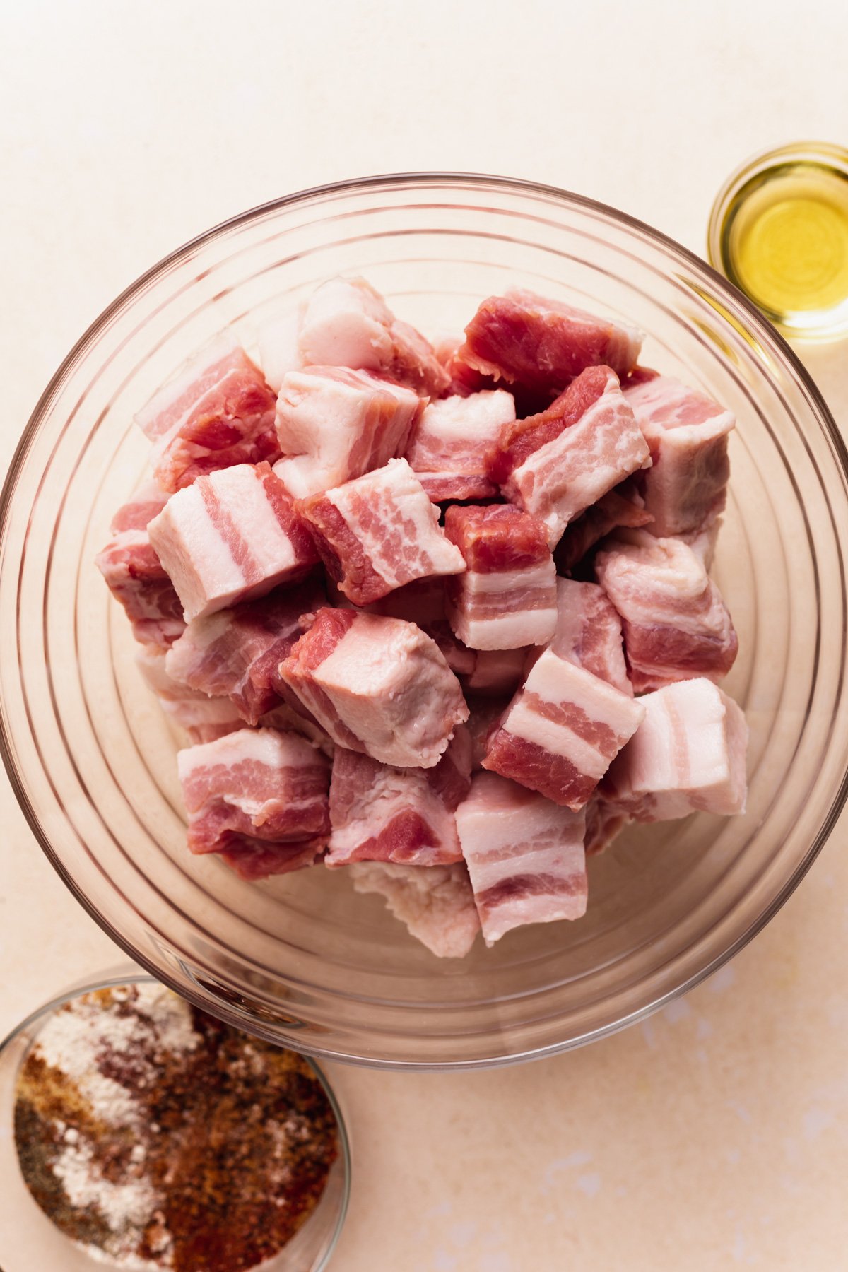 Bowl of cubed pork belly with small bowls of oil and pork dry rub next to it.