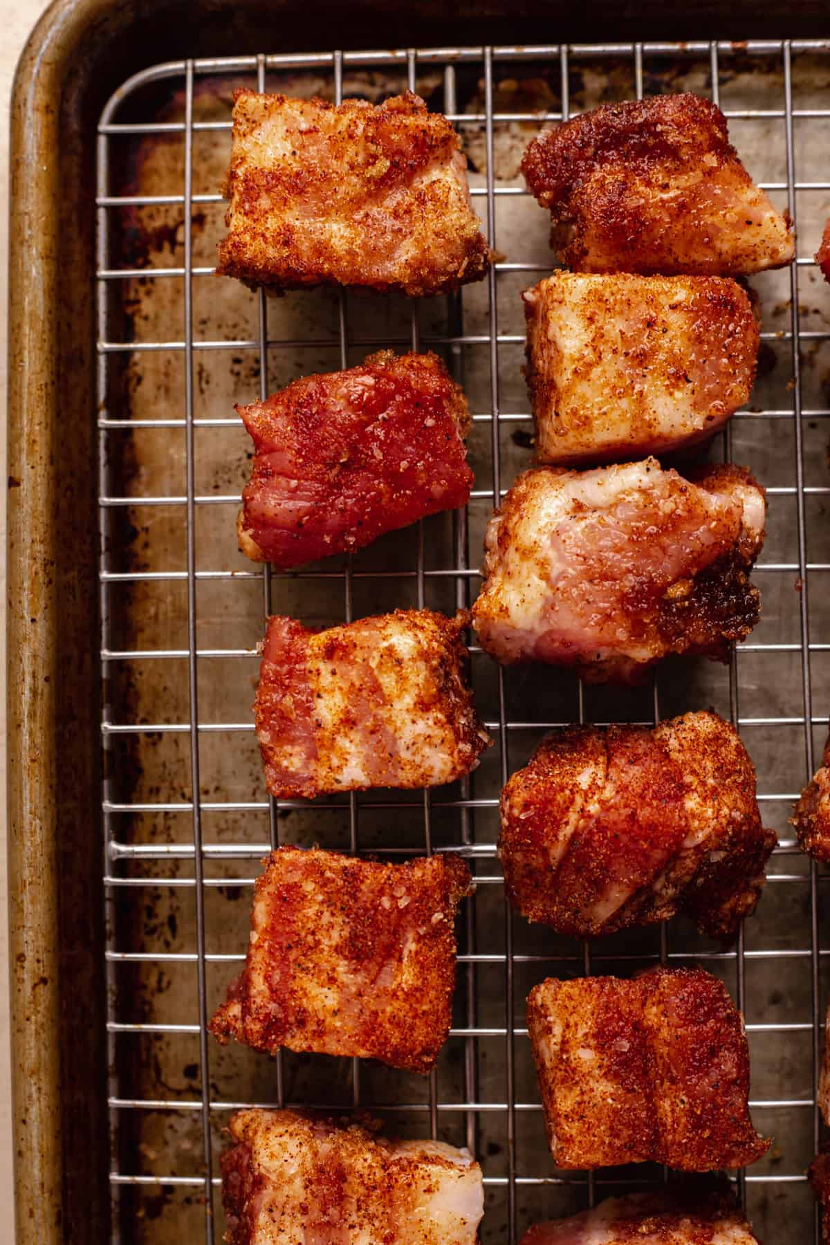 Seasoned cubes of pork belly laid out on a wire rack over a baking sheet.