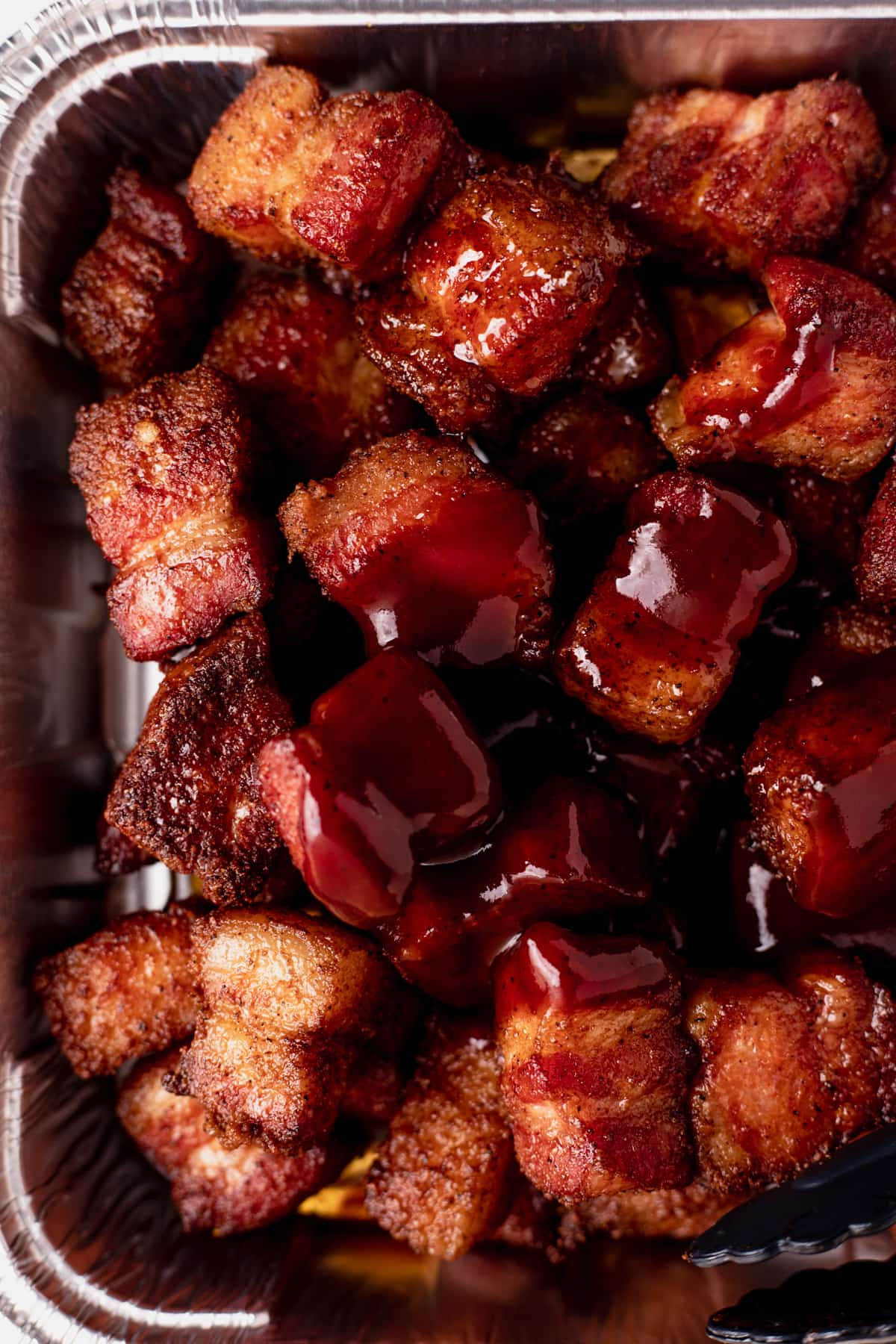 Smoked cubes of pork belly in an aluminum baking tin drizzled with bbq sauce.