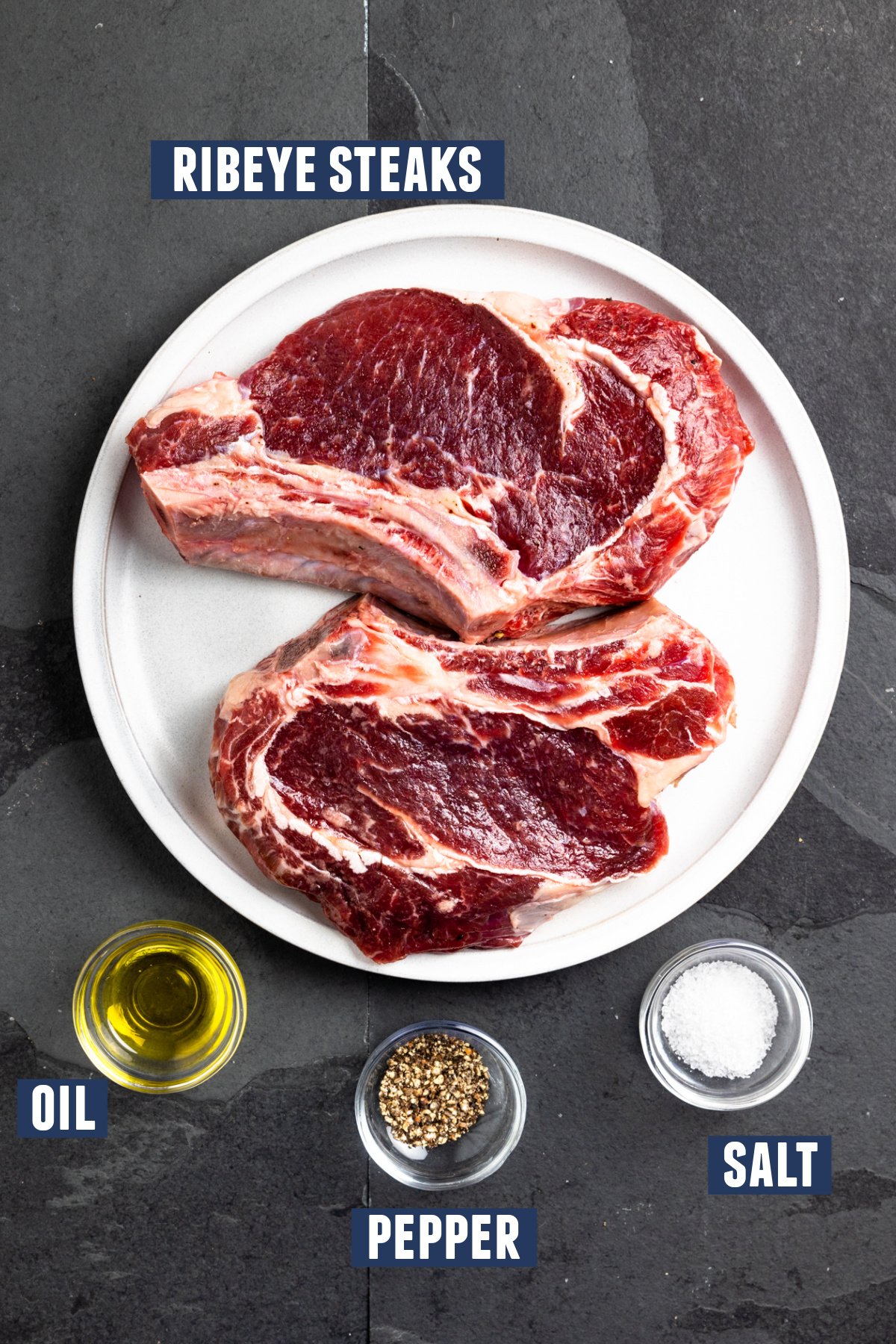 Plate of ribeyes, a small bowl of oil and small bowls of salt and pepper set out to prepare ribeyes for smoking.