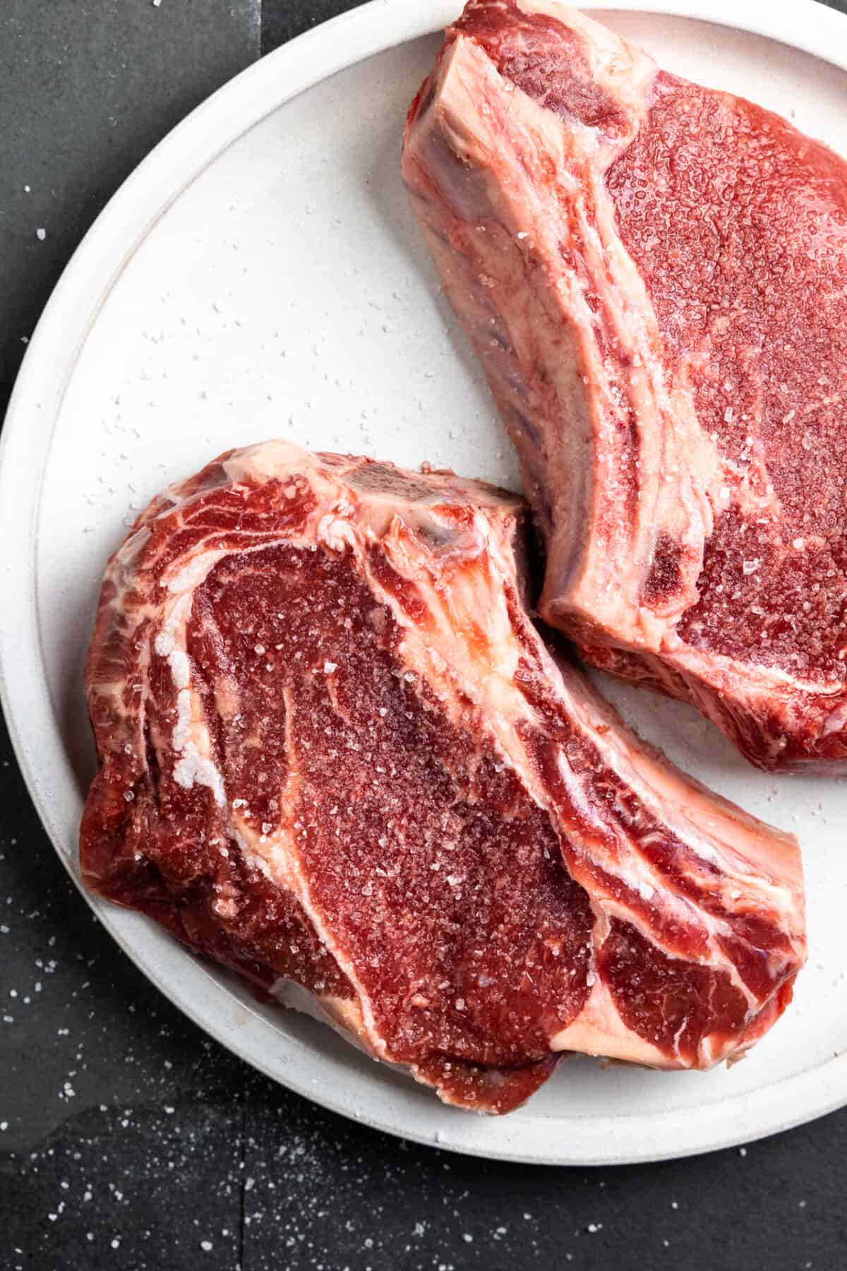 Raw ribeye steaks with salt on a white plate.