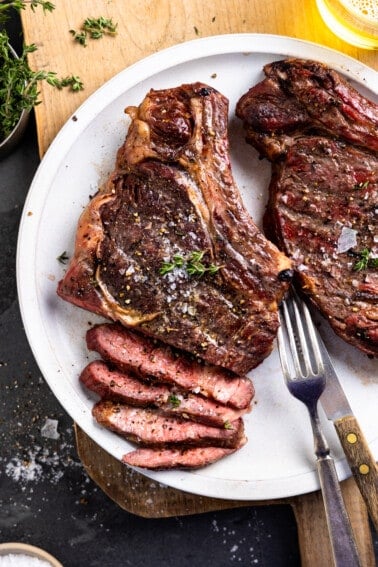 White plate with two smoked ribeyes, a steak knife and a fork. One ribeye is sliced part way.