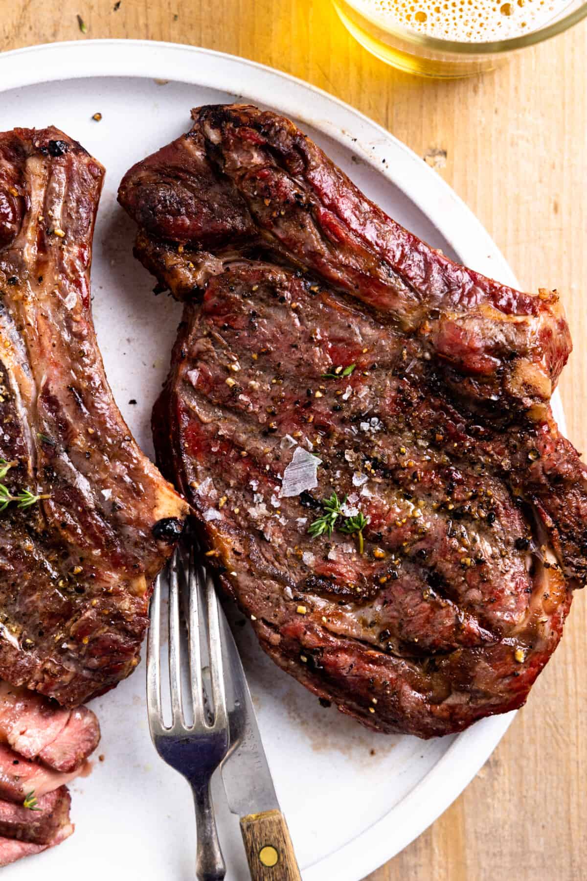 Smoked ribeyes on a white plate sprinkled with flaky salt and a small amount of thyme.