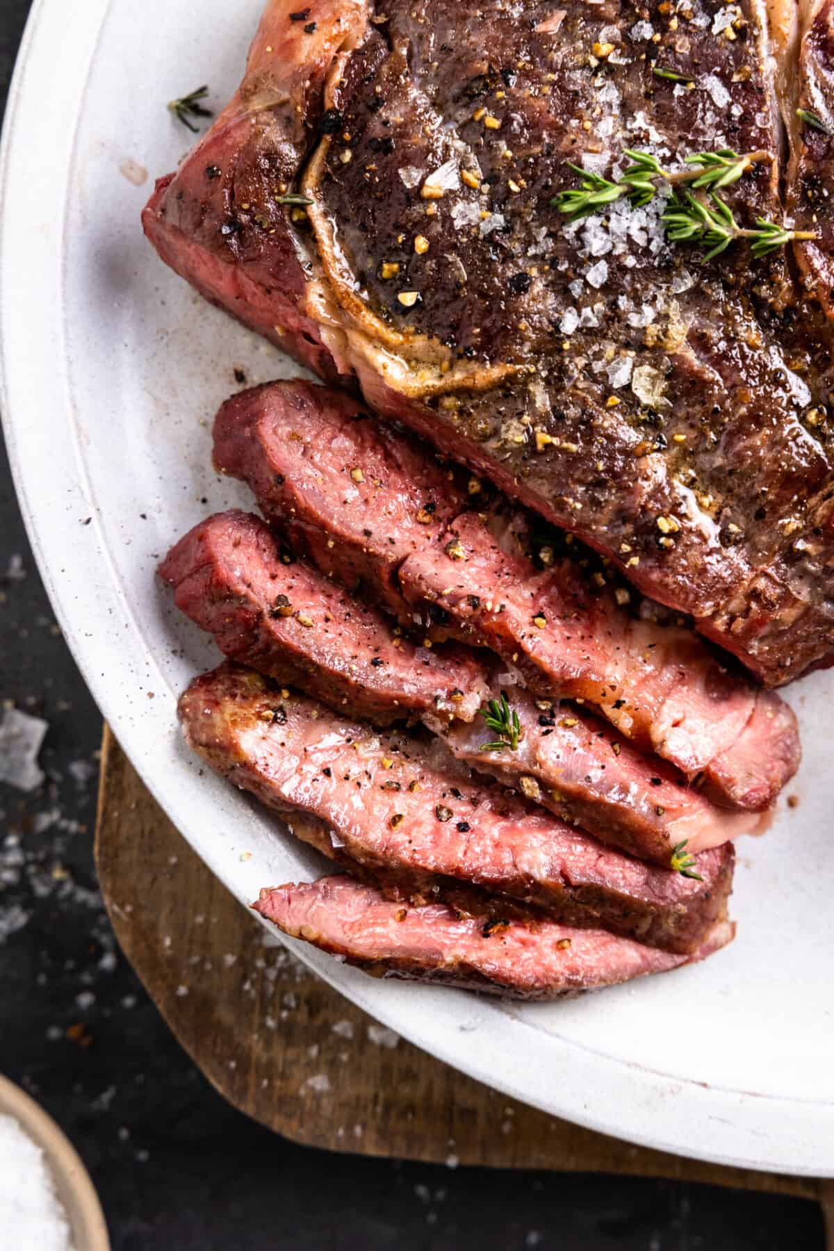 Sliced ribeye topped with flaky salt and thyme, showing a pink center.