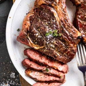 Smoked ribeye on a white plate with a portion sliced showing pink middle.