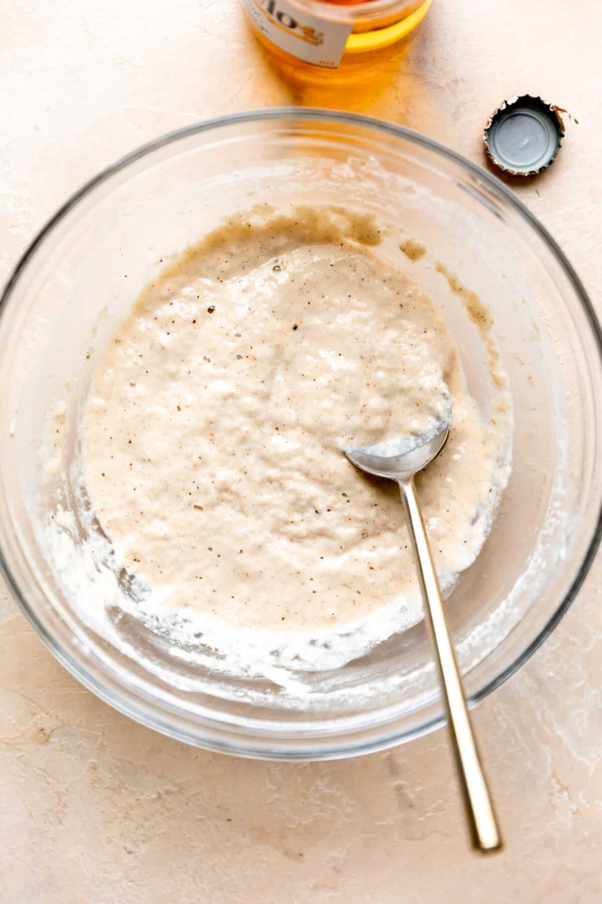 Mixed together beer batter in a glass bowl and a gold spoon.