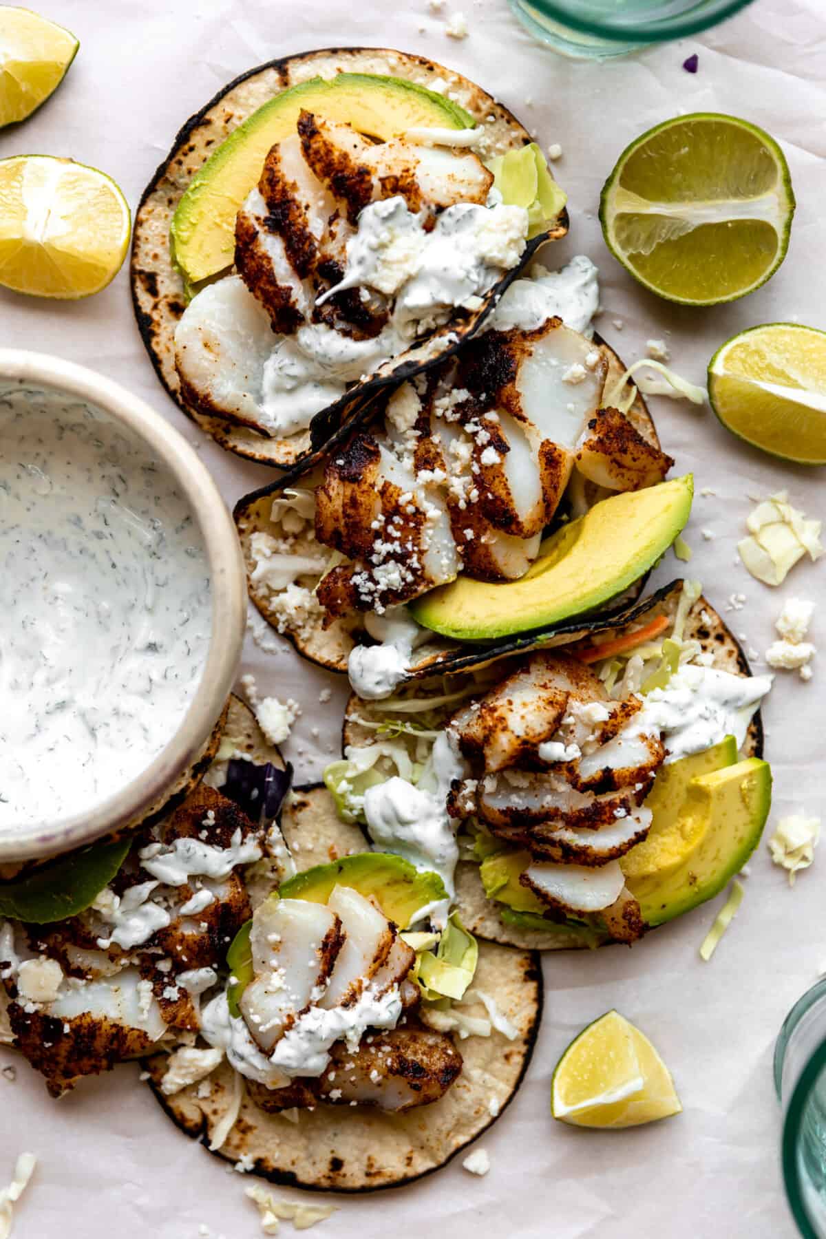 Grilled fish tacos served with a bowl of cilantro lime crema on the side and lime wedges. 