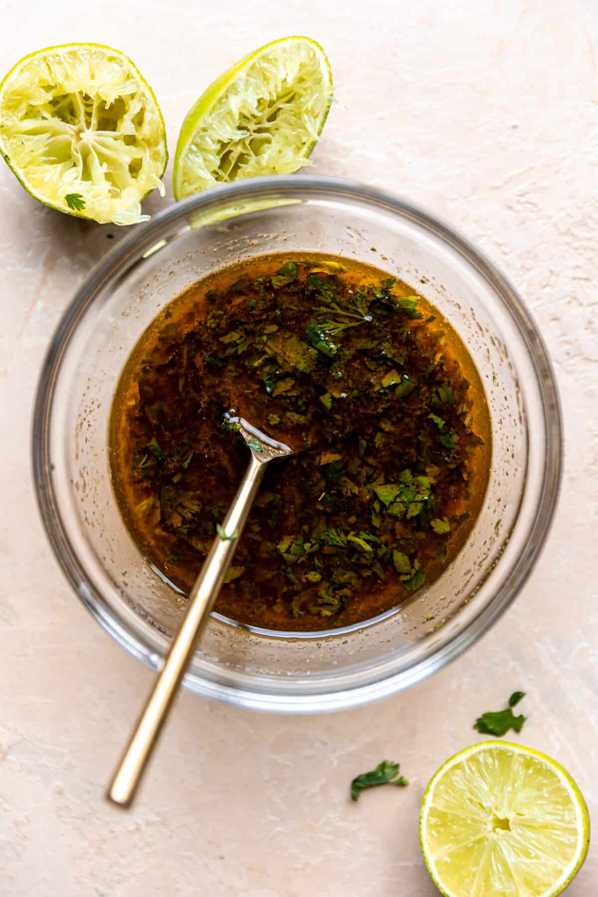 Marinade mixed together in a glass bowl with juiced limes on the side. 