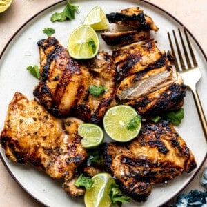 Plate of grilled chicken with lime halves and wedges.