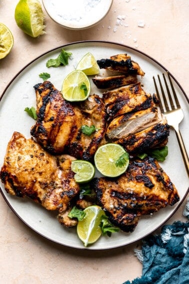 Plate of grilled chicken with lime halves and wedges.