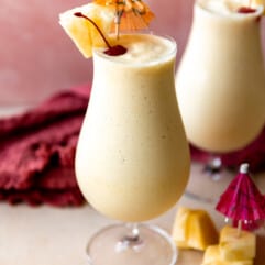 Glasses filled with smooth and creamy frozen pina colada topped with dark red cherries and wedges of pineapple.