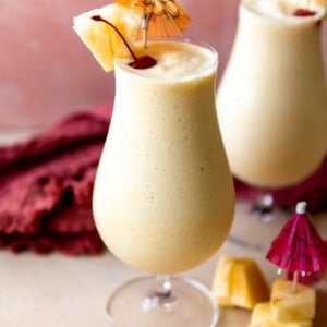 Glasses filled with smooth and creamy frozen pina colada topped with dark red cherries and wedges of pineapple.