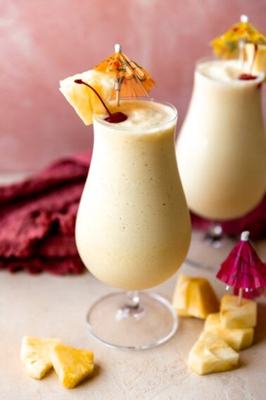 Glasses filled with smooth and creamy frozen pina colada topped with dark red cherries and wedges of pineapple.