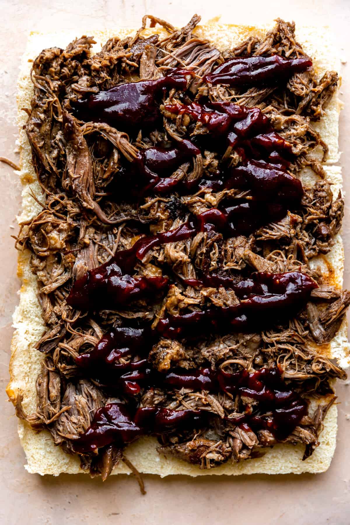 Bottom slider buns topped with pulled pork and bbq sauce.