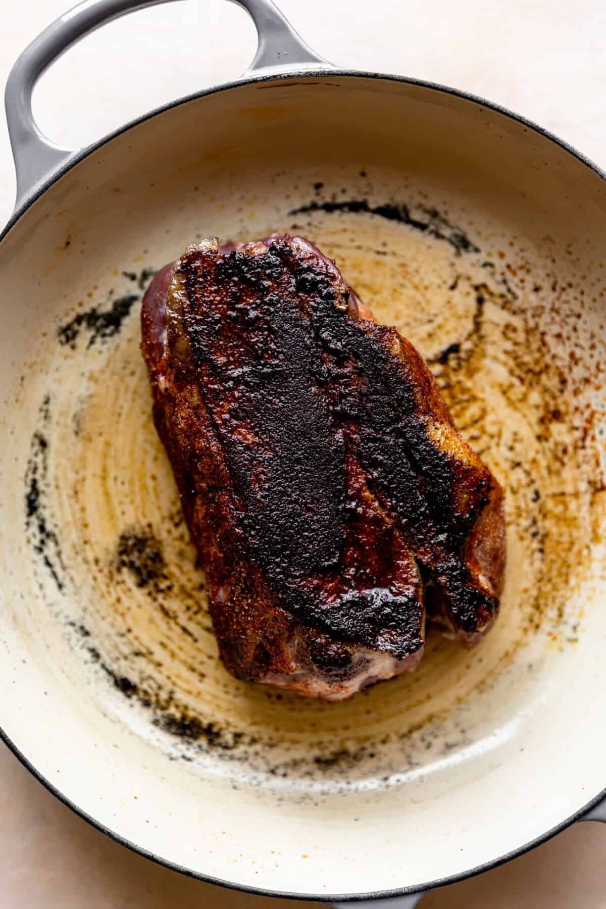 Pork shoulder roast being seared in a cast iron skillet. 