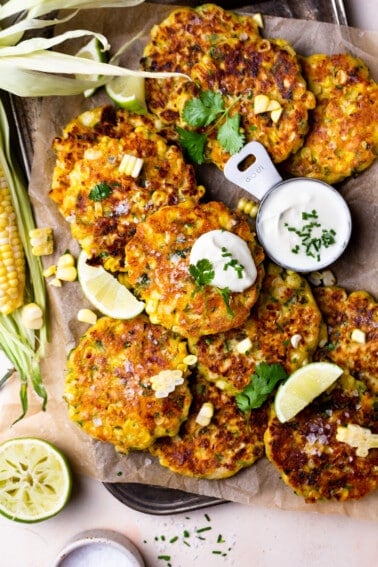 Corn fritters on a tray with sour cream served in cups.