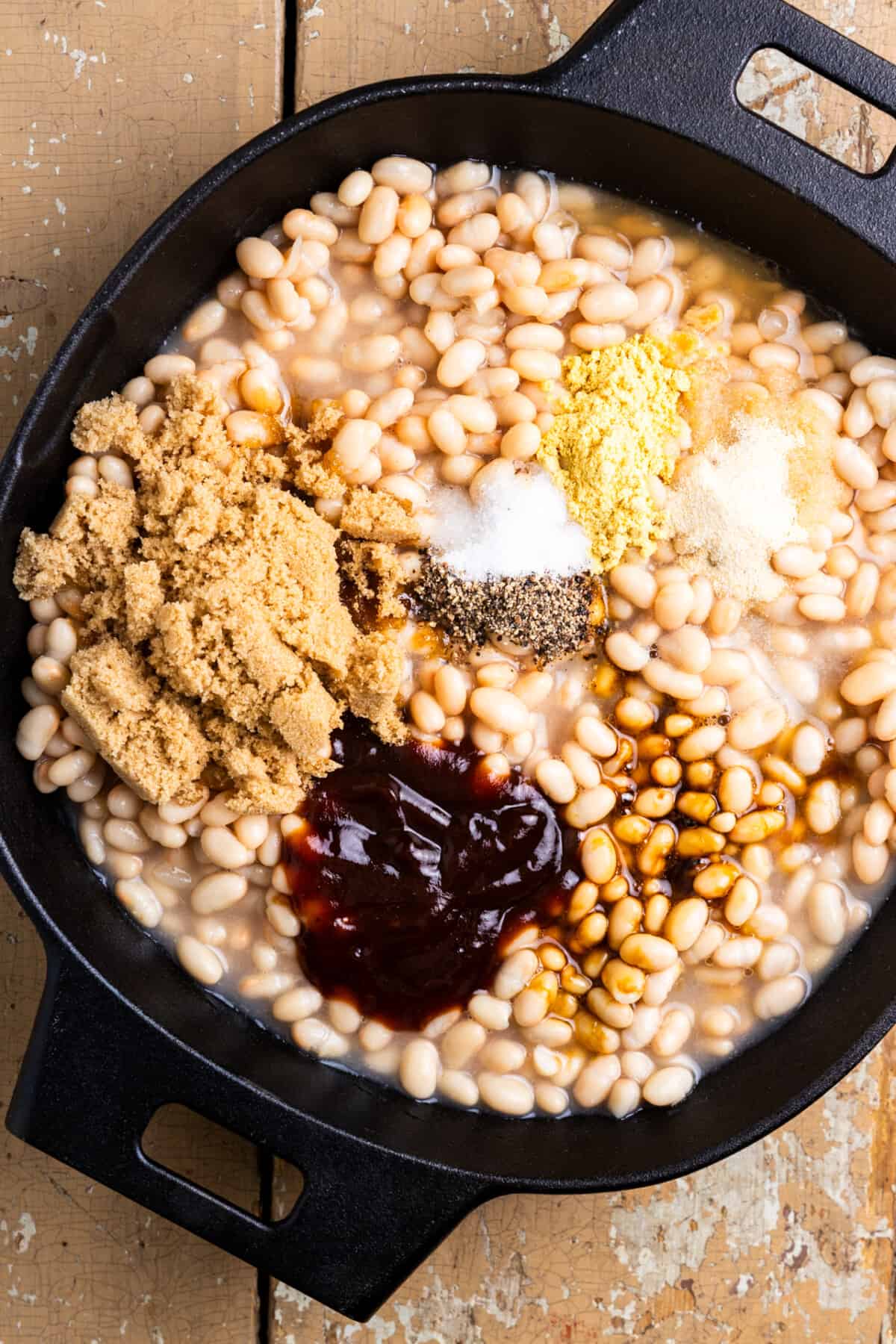 Beans in a cast iron skillet with ingredients on top to stir in for flavor.