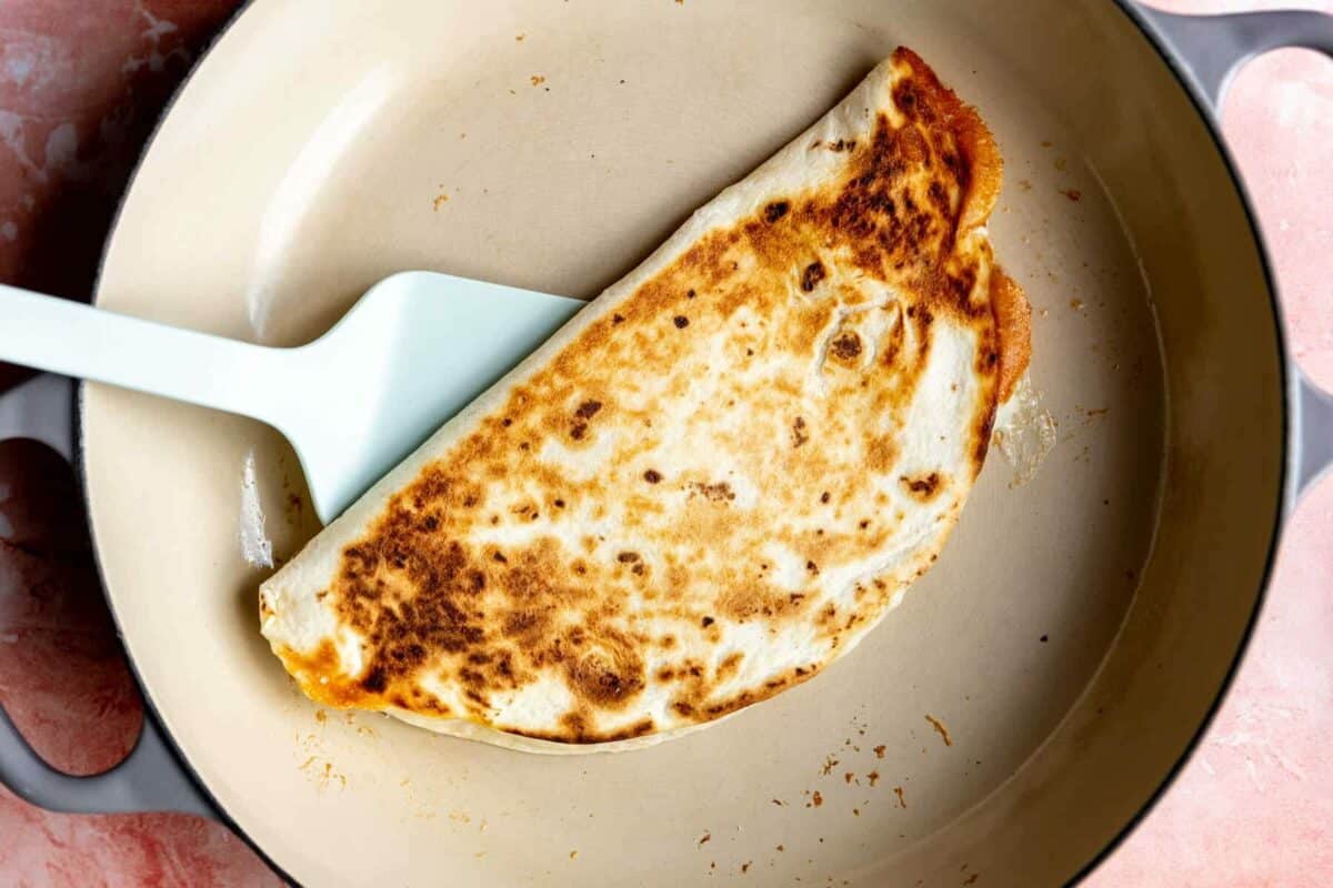 White spatula flipping a browned flour tortilla filled with cheese.