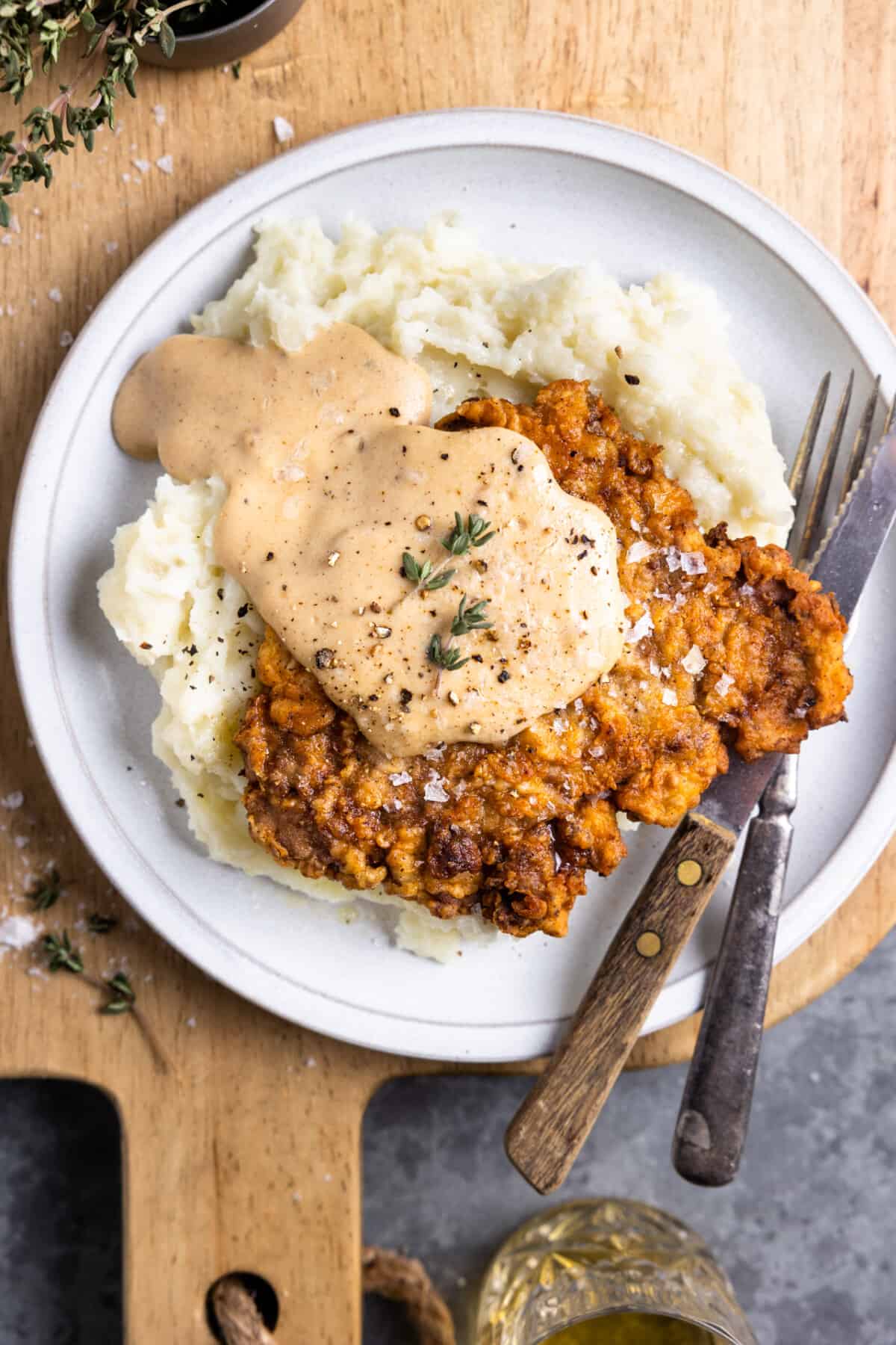 Plate of chicken fried steak on mashed potatoes topped with white cream gravy.