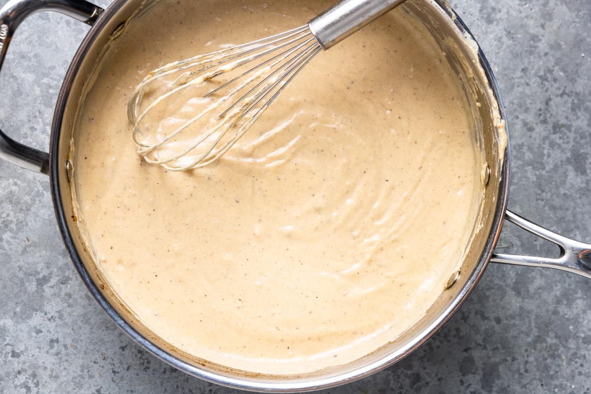 Skillet with creamy white gravy and a whisk. 