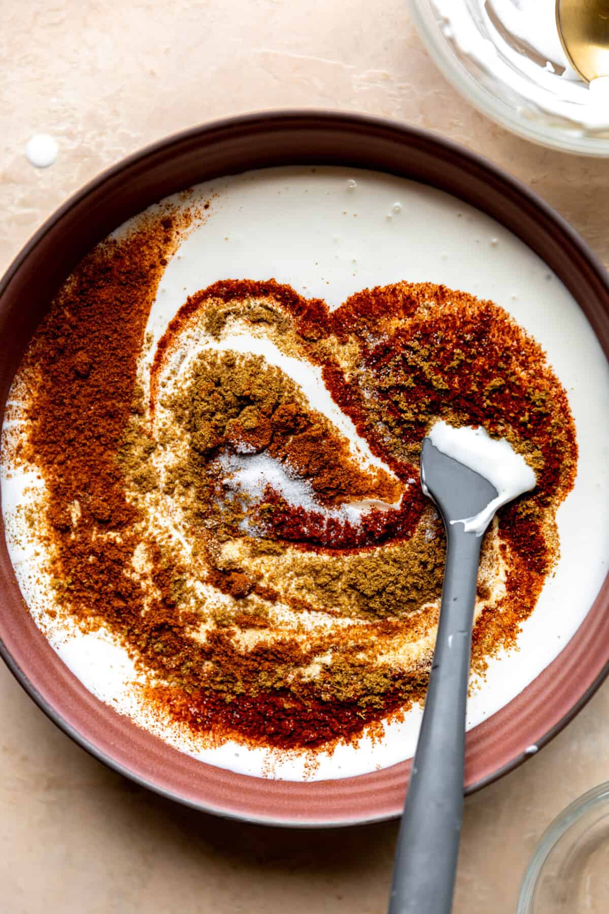 Seasoning blend being added to a bowl of cream sauce. 