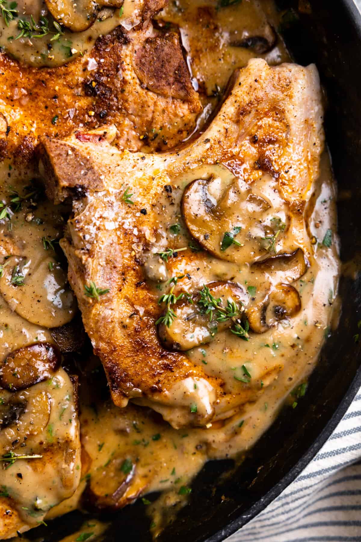 Up close of a pork chop with cream of mushroom soup garnished with parsley.