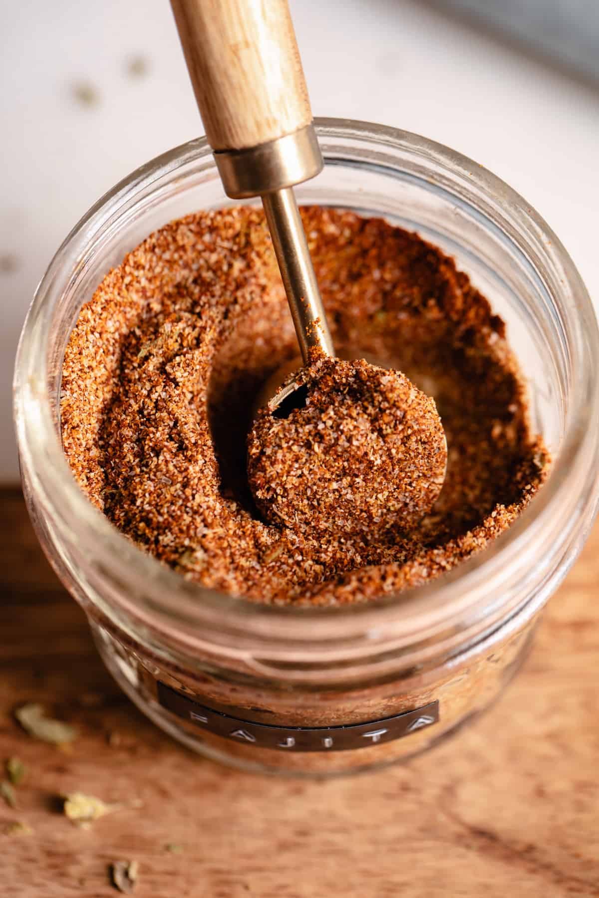 Jar filled with red spice mix with a wooden handled teaspoon scooping it up. 