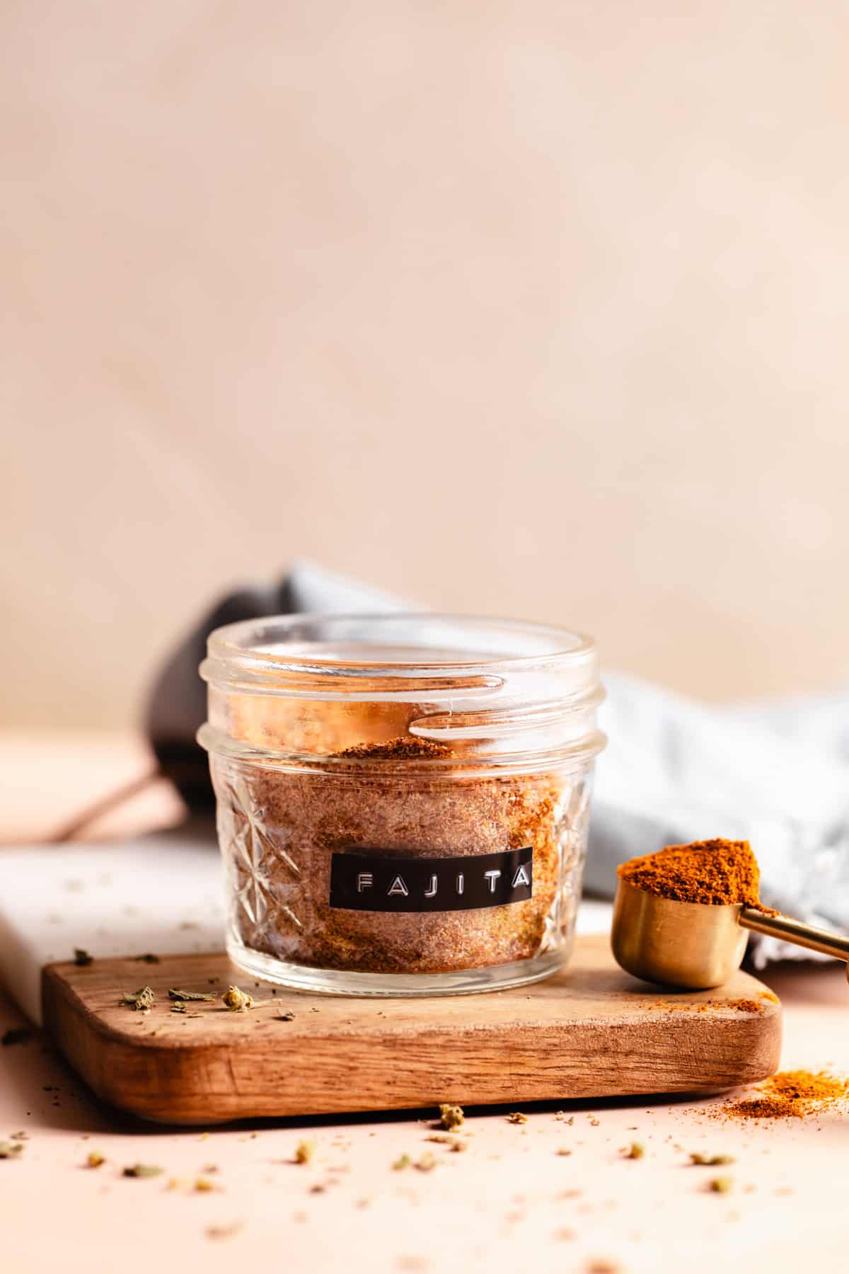 Jar labeled as fajita on a small cutting board with a wooden teaspoon on the side filled with red spices. 