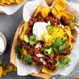 Boats of Frito pie served with sour cream, grated cheese, diced onion and slices of jalapeño.