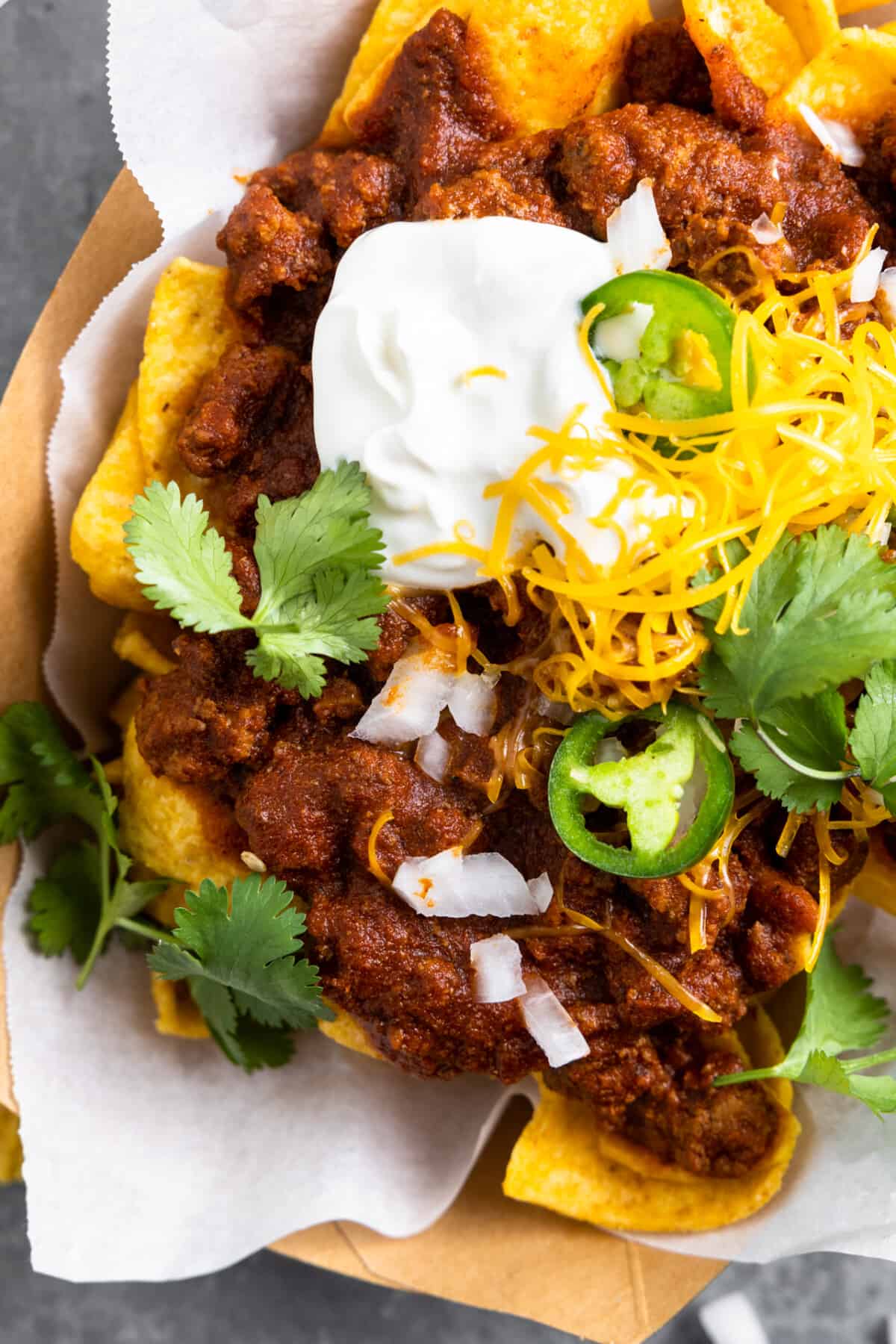 Ground beef chili on top of Fritos for a Texas style Frito pie served in a cardboard boat with sour cream.