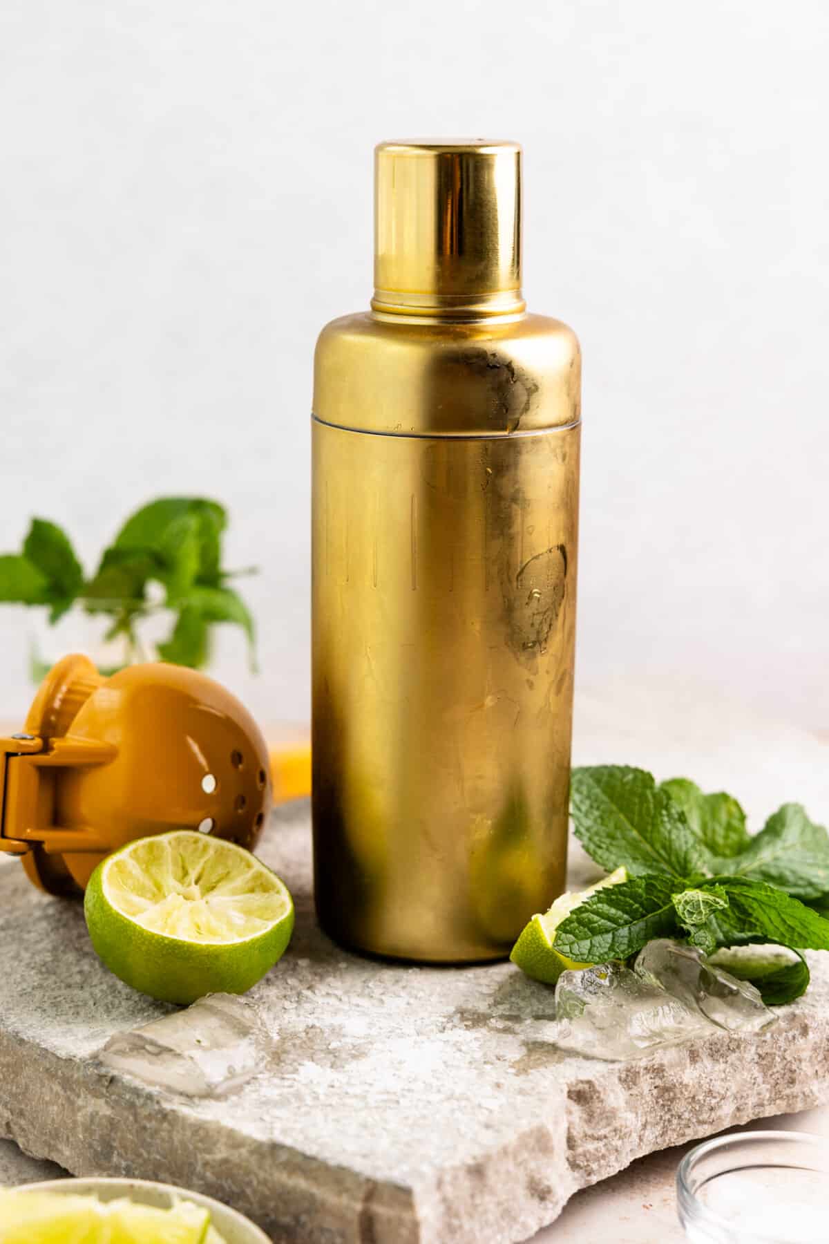 Gold cocktail shake surrounded by mint leaves and lime.