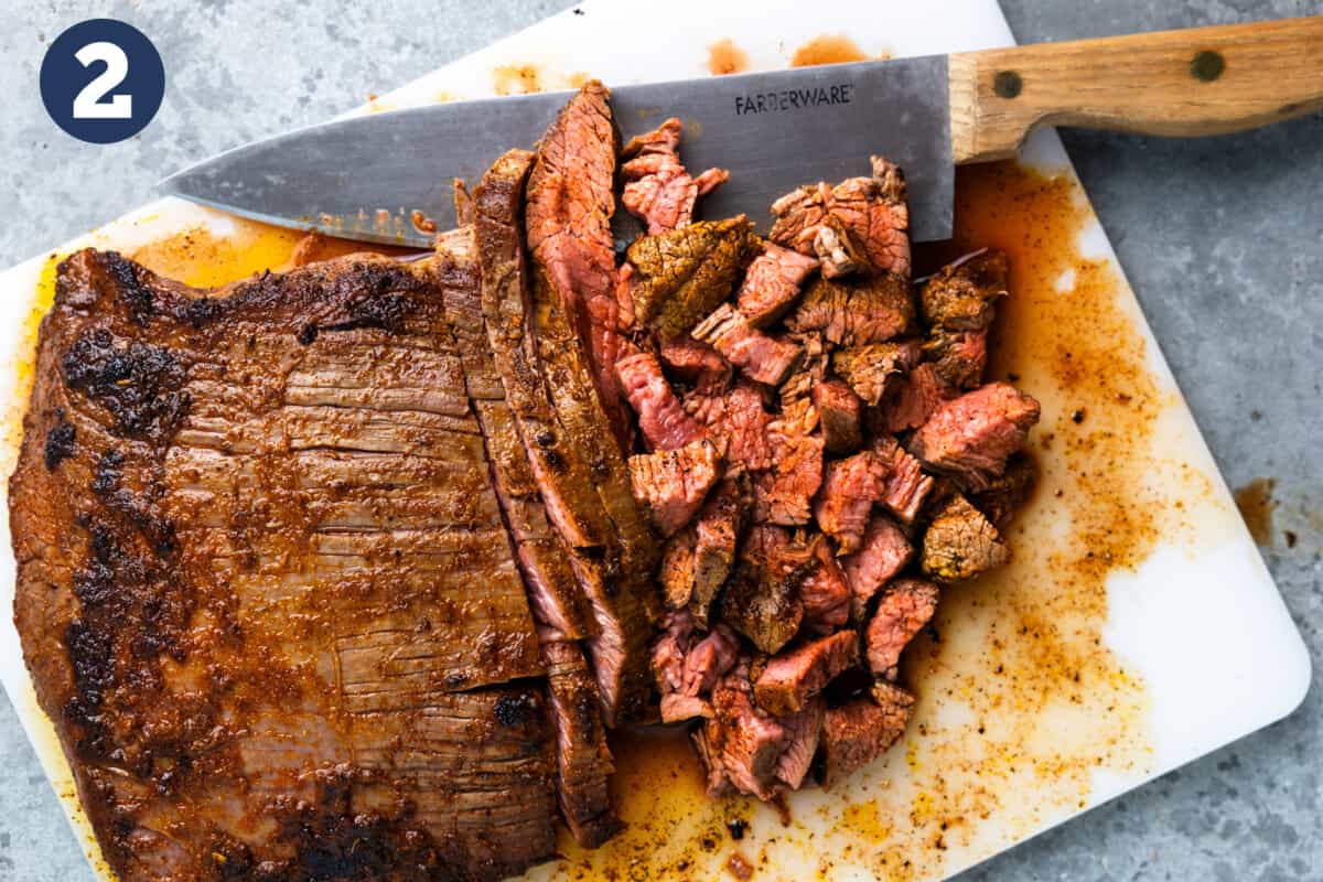 Cooked skirt steak being chopped up on a white cutting board.