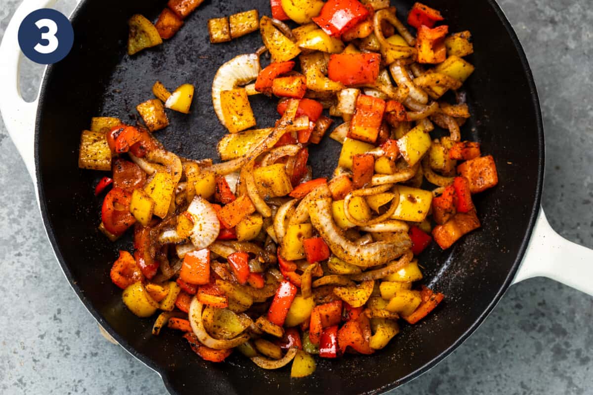 Fajita veggies being cooked in a skillet. 
