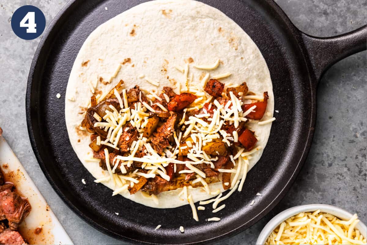 A flour tortilla on a comal with half the tortilla topped with shredded cheese, steak and fajita veggies.