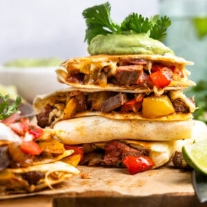 Stack of quesadillas with steak and fajita veggies on a wooden cutting board.