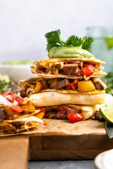 Stack of quesadillas with steak and fajita veggies on a wooden cutting board.
