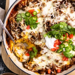 White baking dish with tamale pie topped with melted cheese, sliced jalapeno, diced tomatoes, sour cream and cilantro.