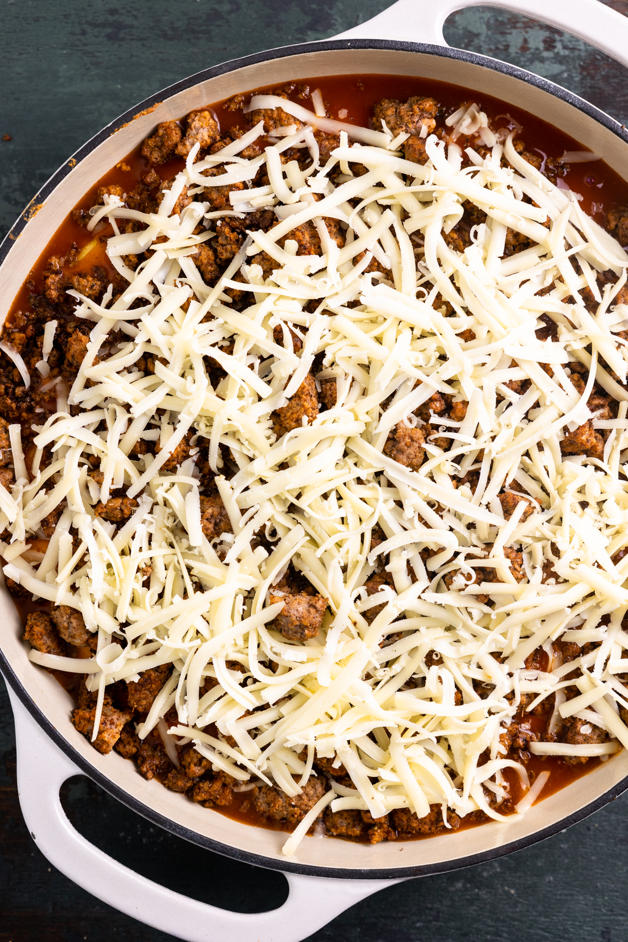 White shredded cheese on top of ground beef over a cornbread mixture for tamale pie. 
